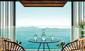 En utomhusplats med ett bord där en kanna och tre glas med vatten står, med utsikt över ett stilla hav och öar på avstånd. (AI-genererad text)