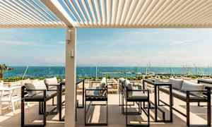 Uteservering med utsikt över havet, med soffor och bord under en pergola. (AI-genererad text)