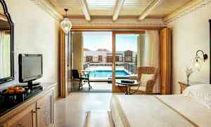 Hotellrum med trädetaljer inklusive en stor säng och en sittgrupp, samt en balkongdörr som leder till en pool. (AI-genererad text)