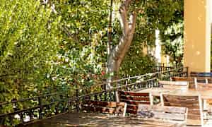 Utomhusbord och stolar står på en skuggig veranda omgiven av grönska. (AI-genererad text)