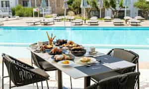 Frukostbord vid en pool med en resort i bakgrunden. (AI-genererad text)