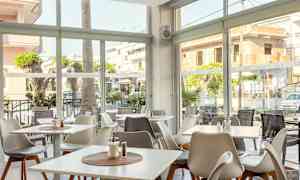 En ljus restaurang med fönster ut mot gatan och utomhusbord. (AI-genererad text)