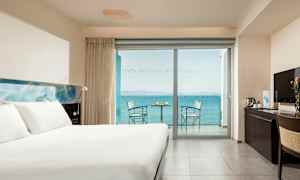 Ett hotellrum med en stor säng, ett skrivbord och en balkong med havsutsikt. (AI-genererad text)