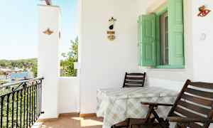 Balkong med två stolar och ett bord, grön fönsterlucka och väggdekoration. (AI-genererad text)