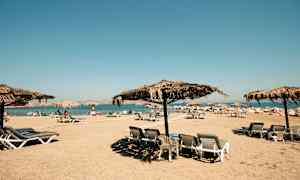 Strand med solstolar och parasoller av halmtak. (AI-genererad text)