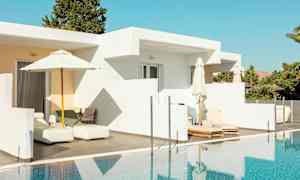 En vit byggnad med uteplats och solstolar vid en pool. (AI-genererad text)