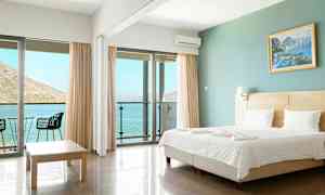Ett hotellrum med en dubbelsäng, glasdörrar som vetter mot en balkong och utsikt över havet. (AI-genererad text)