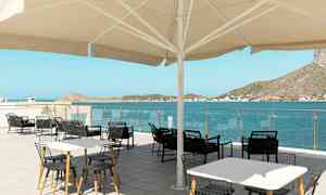 Uteservering med bord och stolar under ett stort parasoll, med utsikt över havet och omgivande kullar. (AI-genererad text)