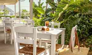 Ett bord med vita stolar, stående utomhus vid grönska, med bok, solglasögon och dryck. (AI-genererad text)