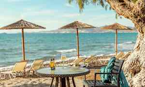 Bord med mat och dryck på en sandstrand med havsutsikt och solstolar. (AI-genererad text)