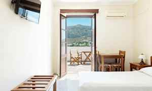 Hotellrum med öppen dörr mot en balkong med utsikt över berg och en by. (AI-genererad text)