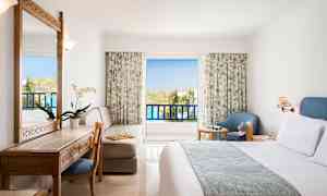 Ett hotellrum med balkong, möbler inklusive säng, skrivbord, stol och fåtölj. (AI-genererad text)