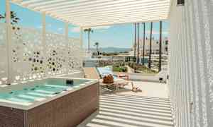 En terrass med jacuzzi, solstolar och utsikt mot palmer och byggnader i bakgrunden. (AI-genererad text)