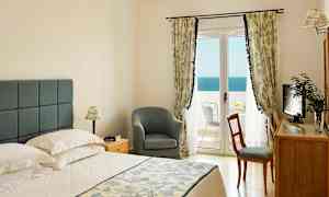 Ett sovrum med en dubbelsäng, en stol, ett skrivbord, och en balkong med utsikt över havet. (AI-genererad text)