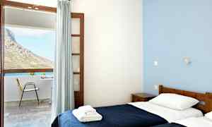 Ett rum med två enkelsängar och stort fönster med utsikt över en uteplats och en bergssluttning. (AI-genererad text)