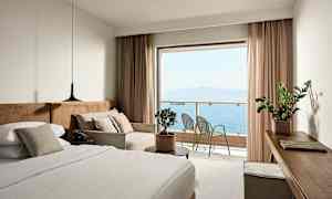 Ett hotellrum med en säng, soffa och utsikt över havet från en balkong. (AI-genererad text)