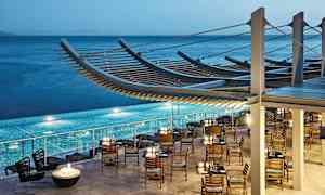 Restaurang med trästolar och bord vid en pool, havet i bakgrunden. (AI-genererad text)