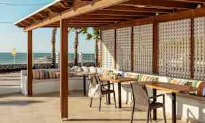 En utomhusterrass med trämöbler, färgglada kuddar och havsutsikt. (AI-genererad text)