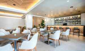 Ett modernt och ljust café med bord och stolar samt en välutrustad bardisk. (AI-genererad text)