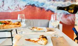 Ett bord med pizza och vinglas, bakgrund med en bild av stranden. (AI-genererad text)