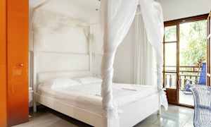 Ett ljust sovrum med en vit himmelssäng och en orange garderob. Ett glasfönster leder ut till en balkong med en stol. (AI-genererad text)