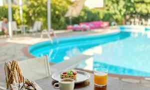 Frukostserverad vid en pool med grönska i bakgrunden. (AI-genererad text)