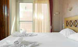 Ett hotellrum med en dubbelsäng, uppställda handdukar och ljusinsläpp genom en glasdörr. (AI-genererad text)