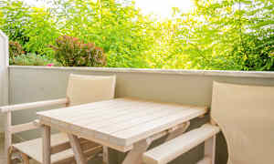 Balkong med ljusa trästolar och bord, omgiven av grönska. (AI-genererad text)