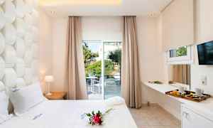 Hotellrum med vit säng, dekorationer och utsikt mot en grönskande terrass genom stora fönster. (AI-genererad text)