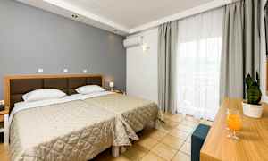 Hotellrum med två enkelsängar, ett skrivbord med en växt och dryck, och stora fönster med ljusa gardiner. (AI-genererad text)