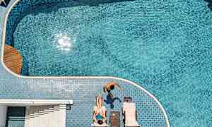 Personer vid en pool, en kvinna ligger på solstol och en man går intill. (AI-genererad text)