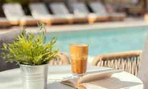 Ett glas iskaffe och en uppslagen bok på ett bord vid en pool. (AI-genererad text)