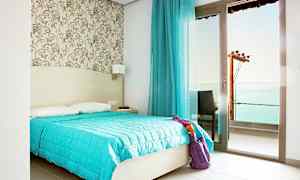 Ett hotellrum med dubbelsäng, blå täcke och en glasdörr som leder till en balkong. (AI-genererad text)