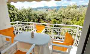 En balkong med utsikt över en trädgård med olivträd och berg i bakgrunden. (AI-genererad text)