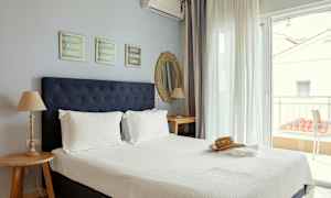 Ett hotellrum med en dubbelsäng, nattduksbord och utsikt över en terrass. (AI-genererad text)