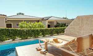 En solstol vid en pool med en stråhatt och en handduk på. I bakgrunden syns bostadshus och vegetation. (AI-genererad text)