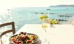 En tallrik med sallad och ett glas vitt vin på ett bord med utsikt över havet. (AI-genererad text)