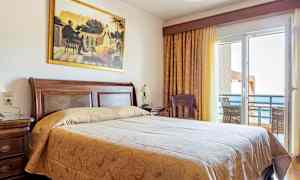 Ett hotellrum med en stor säng, trädetaljer och en balkong med havsutsikt. (AI-genererad text)