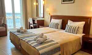 Hotellrum med två enkelsängar, skrivbord och utsikt över havet från balkongen. (AI-genererad text)