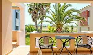 Vy från en terrass med två stolar och ett bord, omgiven av palmer och en lummig trädgård. (AI-genererad text)