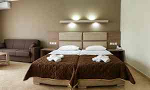 Hotellrum med två enkelsängar och en brun soffa. (AI-genererad text)