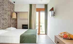 Ett hotellrum med en dubbelsäng, ett tegelvägg, en TV, en balkong och en korg med frukt på ett bord. (AI-genererad text)