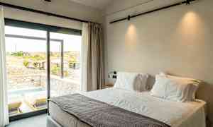 Hotellrum med stor säng vid ett fönster som vetter mot en uteplats med solsängar och liten pool. (AI-genererad text)