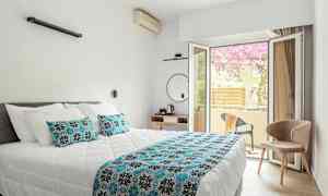 Ett hotellrum med en dubbelsäng och ett öppet glasfönster mot en balkong. (AI-genererad text)