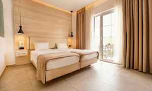 Två enkelsängar i ett ljust rum med stora glasdörrar och beige gardiner. (AI-genererad text)