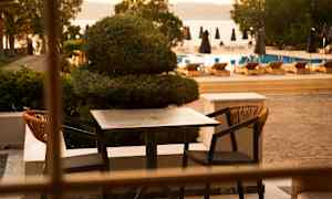 Ett utomhusbordsset med två stolar vid en terrass, med en pool och solstolar i bakgrunden. (AI-genererad text)