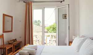 Ett ljust sovrum med vita väggar, en säng med vit bäddning och en balkong utanför glasdörrar. (AI-genererad text)