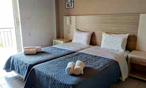 Rummet har två enkelsängar med blå överkast och vita kuddar, samt hoprullade handdukar placerade på sängen. (AI-genererad text)