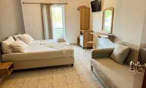 Ett hotellrum med en säng, soffa, skrivbord och garderob. Fönstret har ljusa gardiner. (AI-genererad text)