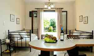 En inomhusmiljö med ett bord med frukt och en vinflaska, två bäddar och en öppen dörr som leder till en trädgård. (AI-genererad text)